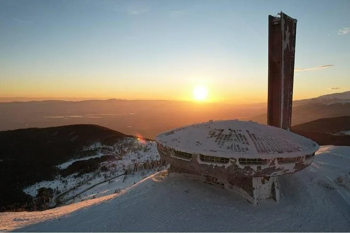 Das schneebedeckte Buzludscha-Denkmal bei Sonnenaufgang auf einem Berggipfel.
